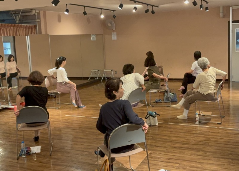 椅子に座りながら体をひねる動きで身体のストレッチを行っています。